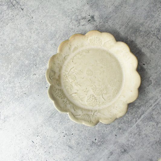 beige round textured plate with scalloped edge on grey background