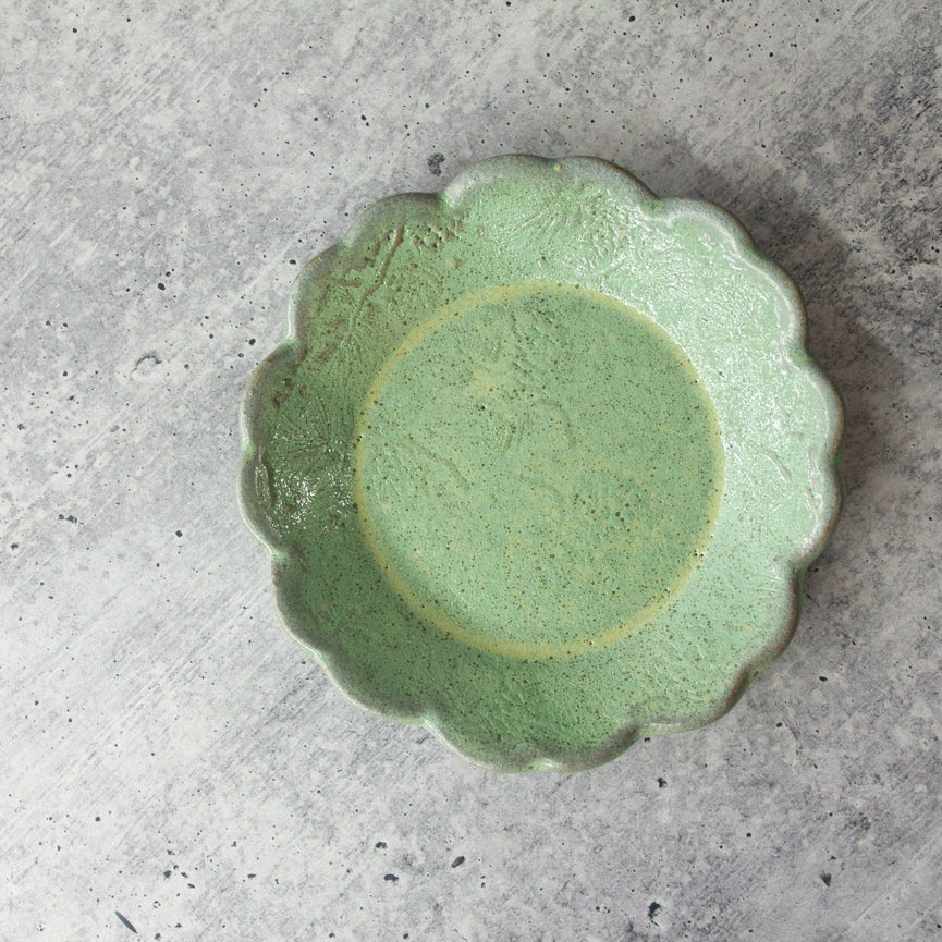 round green ceramic plate with texture and scalloped edge on grey background