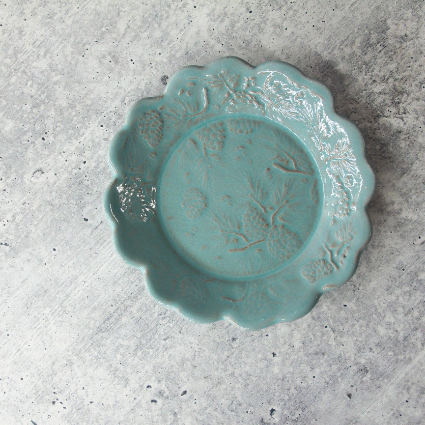 turquoise ceramic plate with scalloped edges and pine cone design