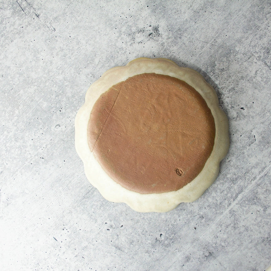 red clay beige round textured plate with scalloped edge on grey background