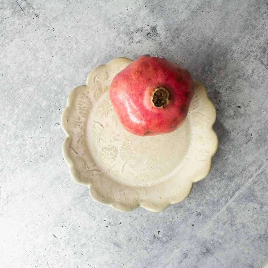beige round textured plate, red fruit with scalloped edge on grey background