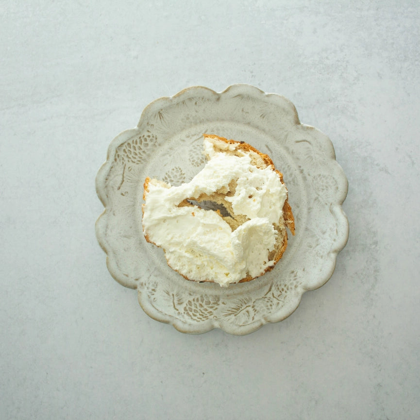 beige white ceramic plate with bagel and cream cheese on grey background
