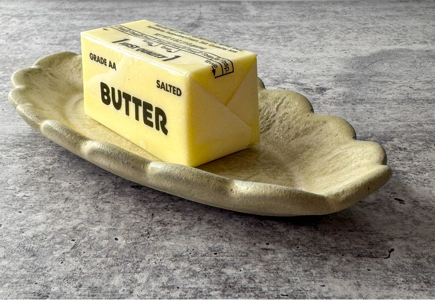 scalloped edge dish with butter stick on gray background