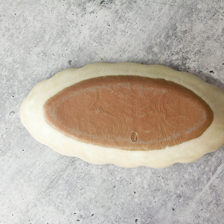 oval shaped plate showing red clay bottom on gray background