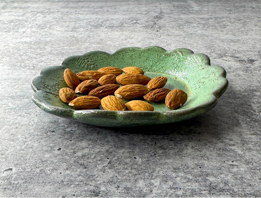 round green ceramic plate with texture, almonds and scalloped edge on grey background