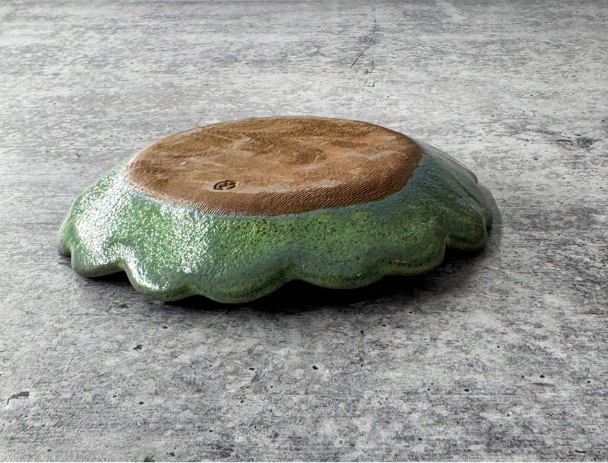 bottom of round green ceramic plate with texture and scalloped edge on grey background