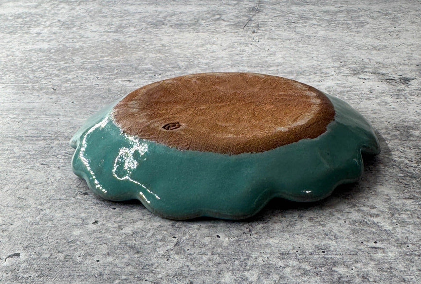red clay bottom of turquoise ceramic plate with scalloped edges  on grey background.