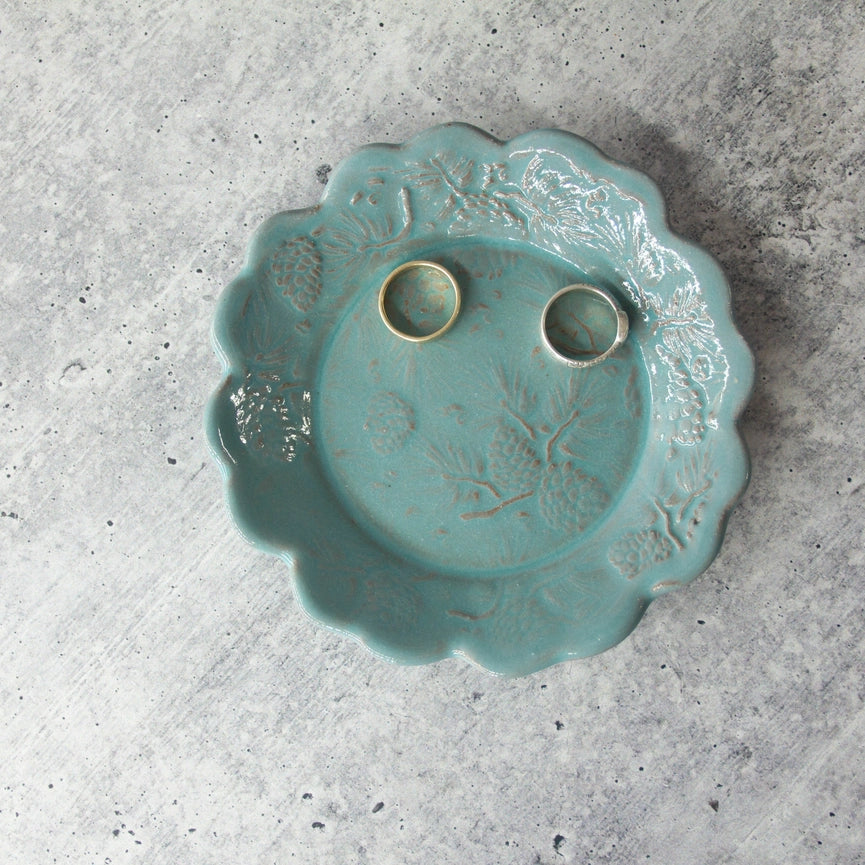 turquoise ceramic plate with scalloped edges and two silver rings on grey background.