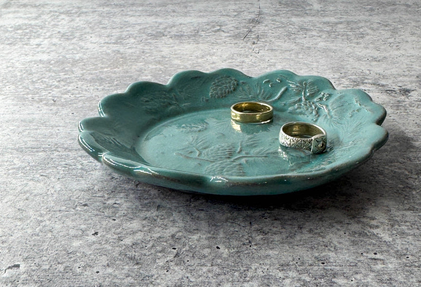 turquoise ceramic plate with scalloped edges and two silver rings on grey background.