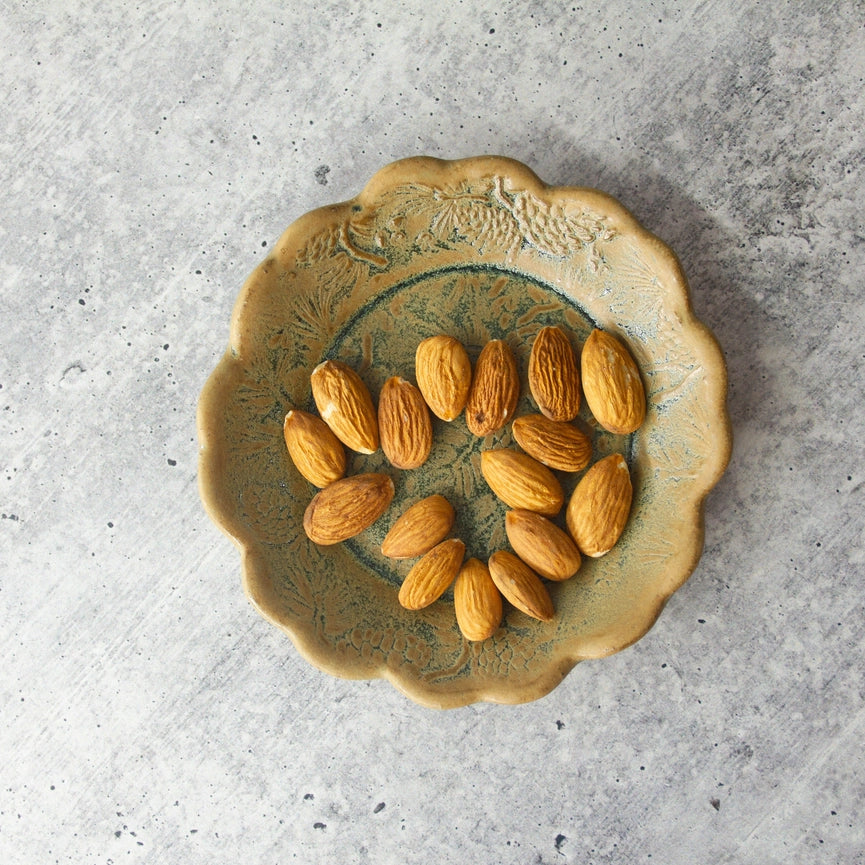 yellow and green scalloped edge plate with almonds on grey background
