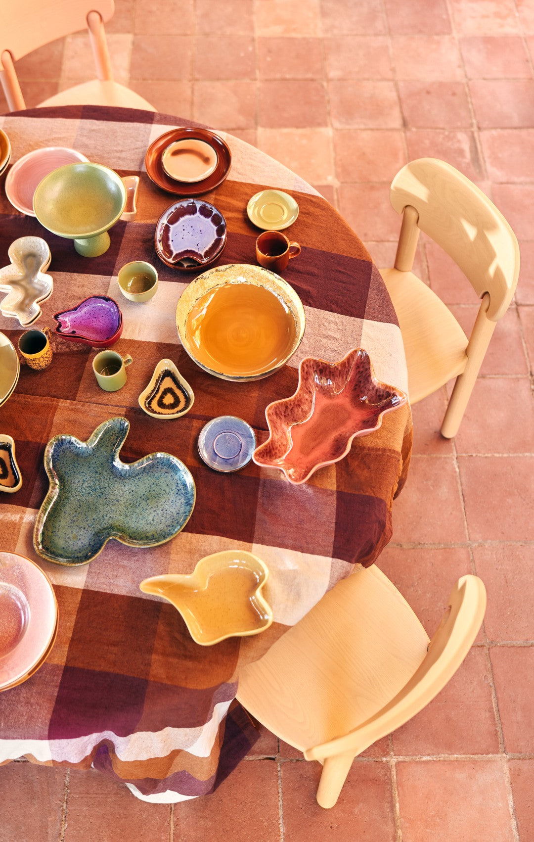 Colorful ceramic plates and bowls on a round wooden table with a checkered tablecloth.