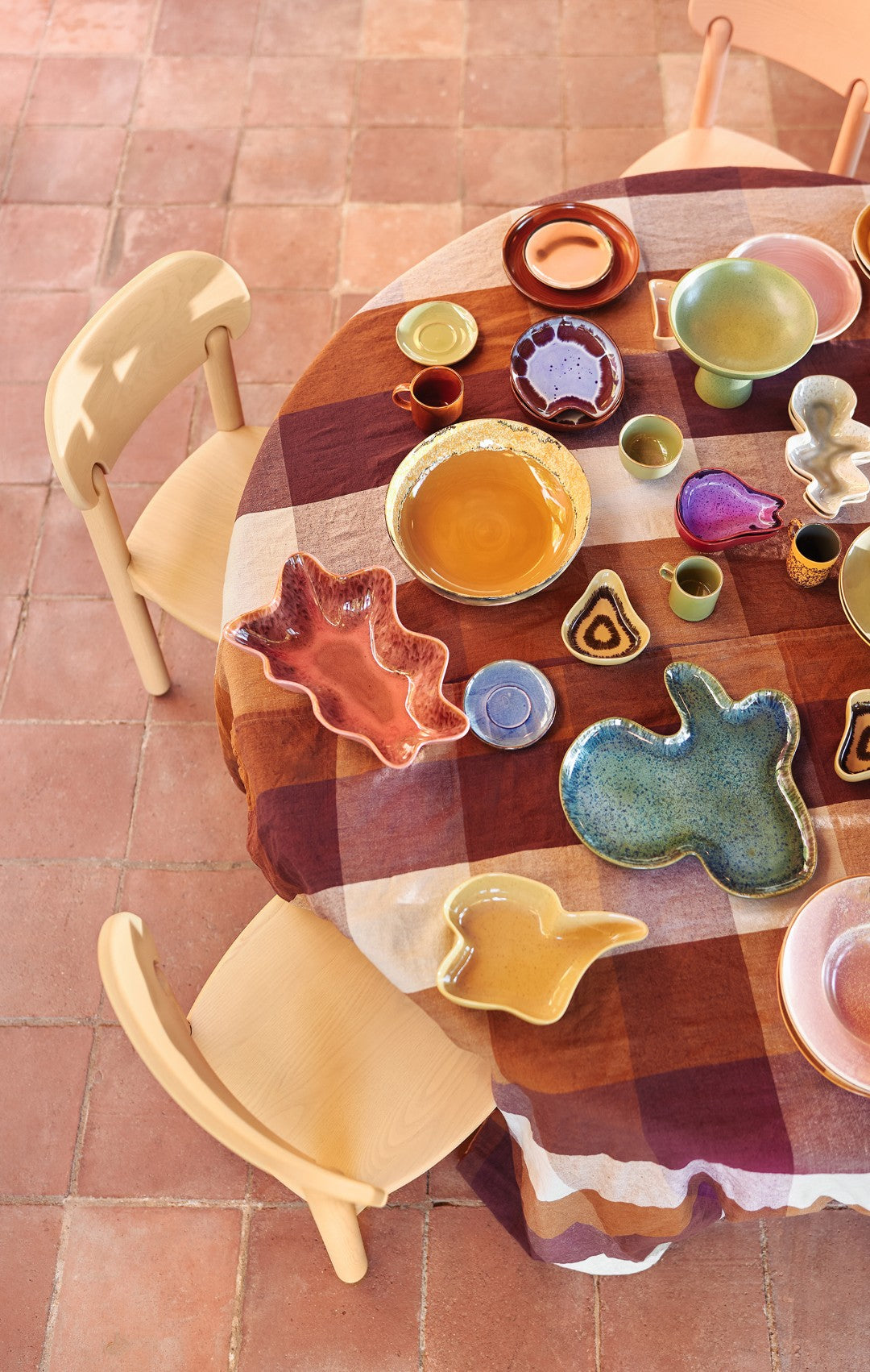 Round wooden table with colorful ceramic plates and platters on a tiled floor.