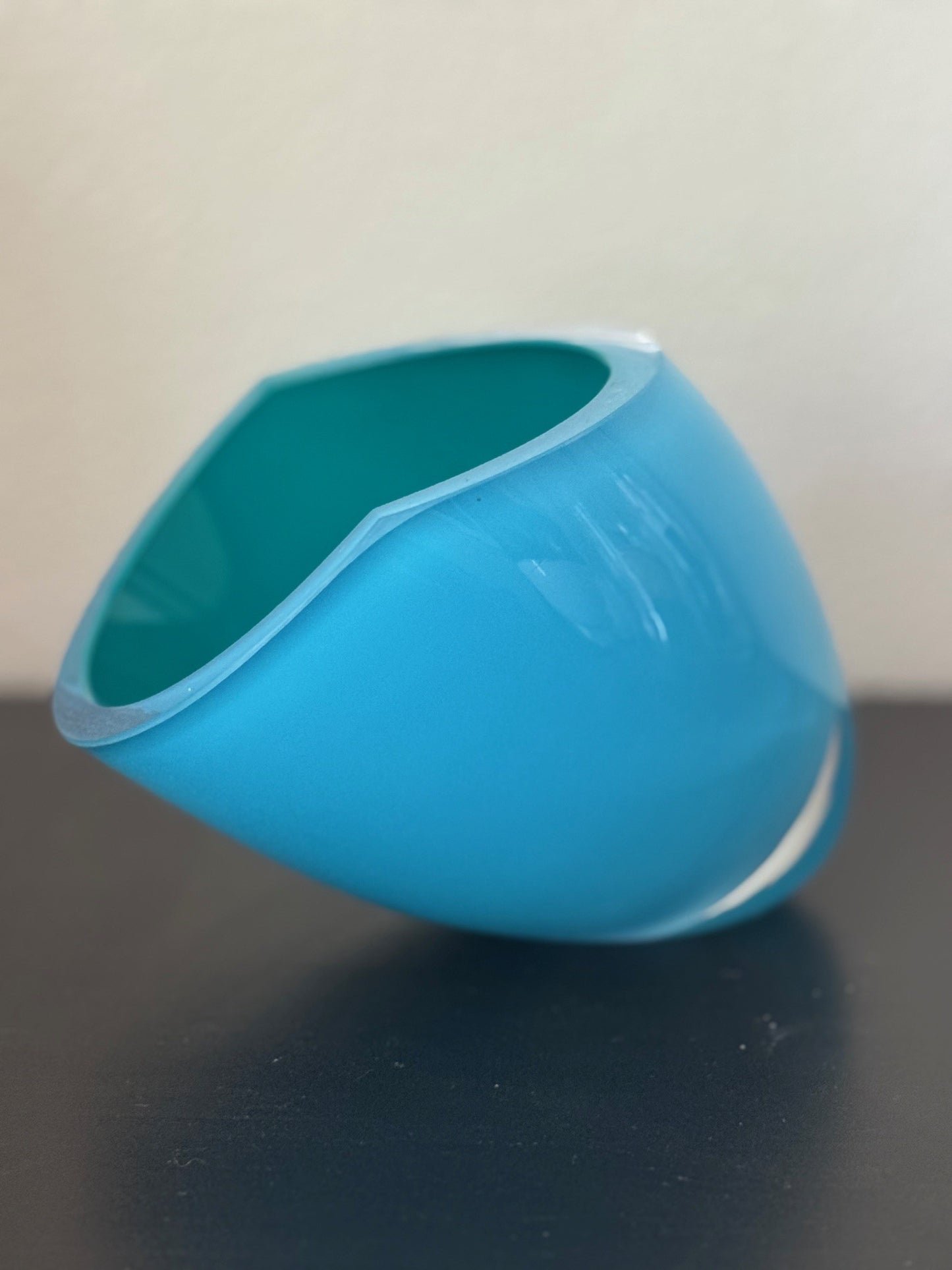 Blue glass object on a dark surface with a light gray background