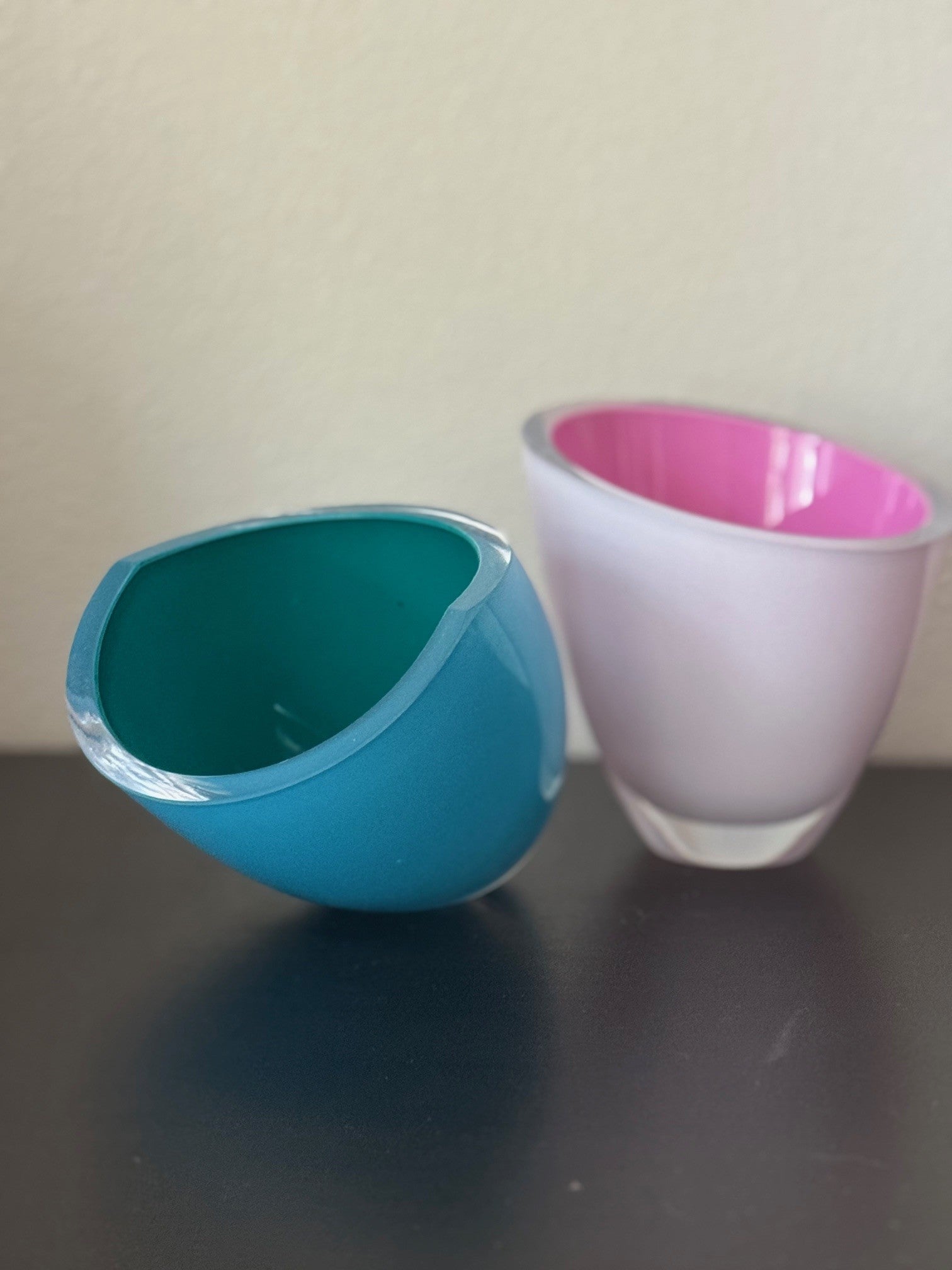 Two colorful glass bowls, one blue and one pink, on a dark surface with a light background.