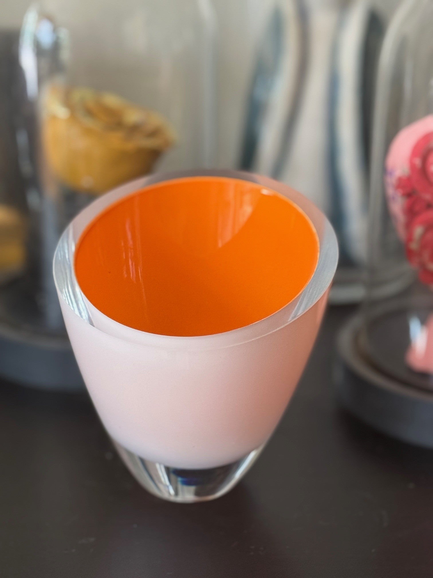 Two-layered dessert in a glass with orange top and white bottom on a dark surface.