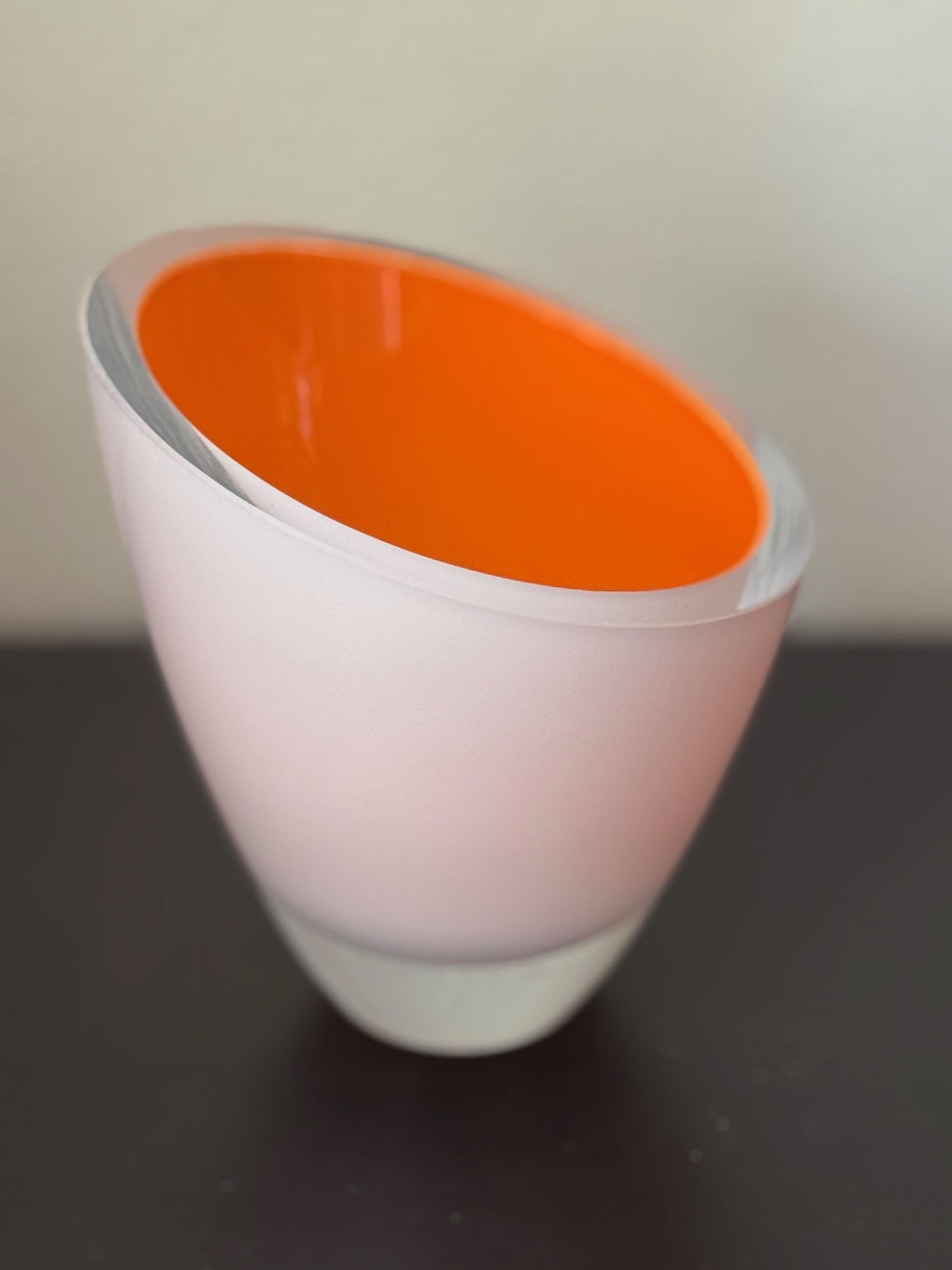 Vase with white base and orange interior on a dark surface