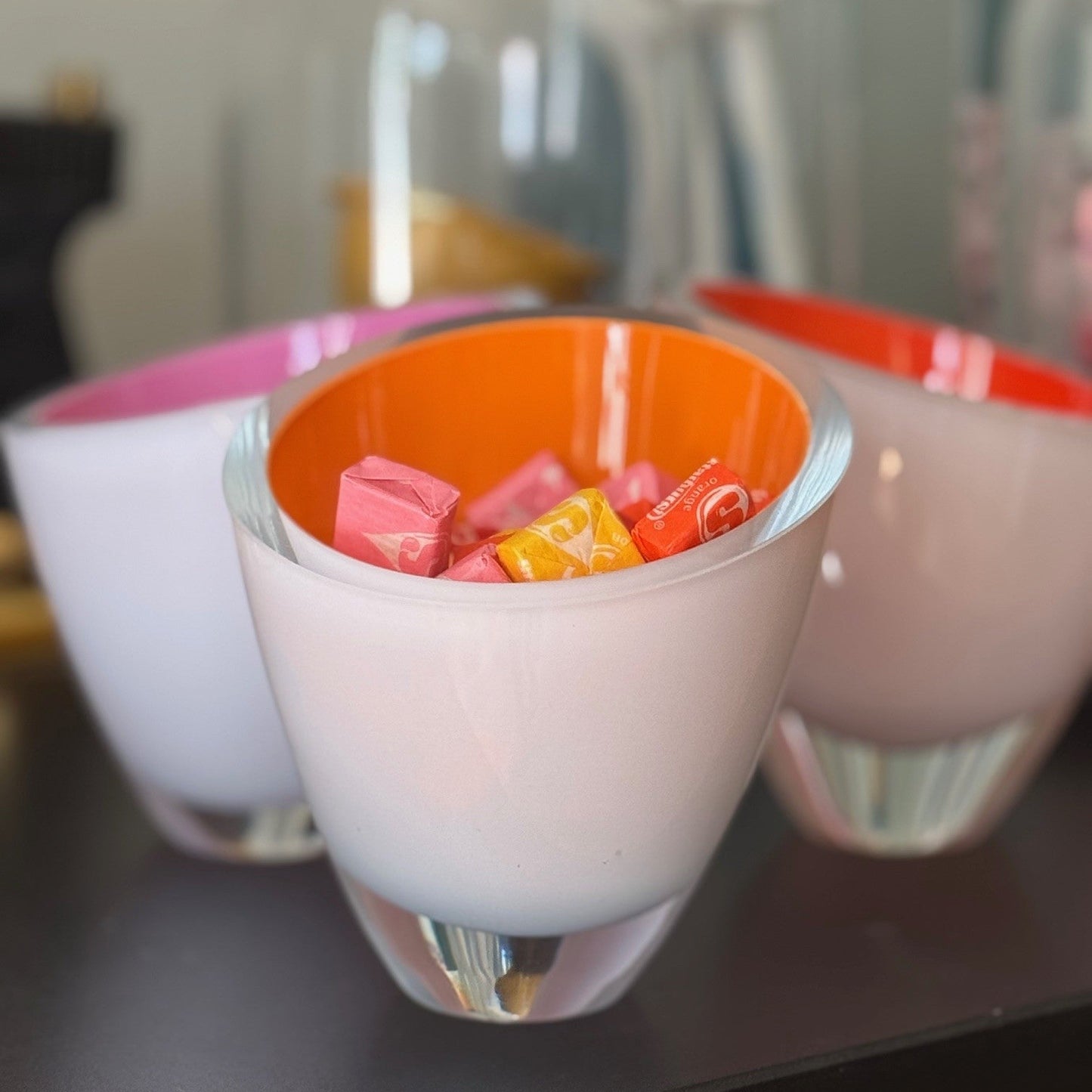 Two mugs with colorful candy inside on a reflective surface.