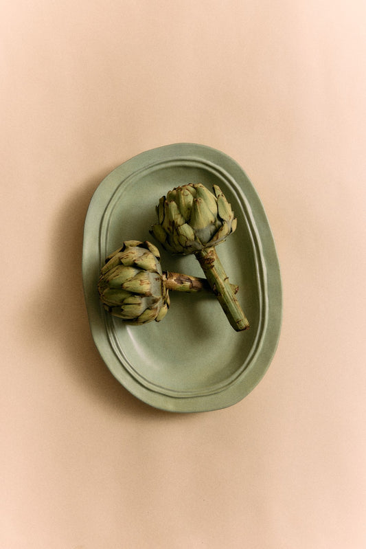 Two artichokes on a green plate against a beige background
