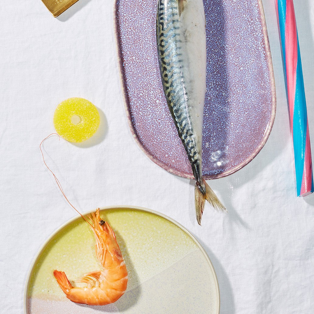 Shrimp and fish on ceramic plates with colorful straws and a yellow object in the background.