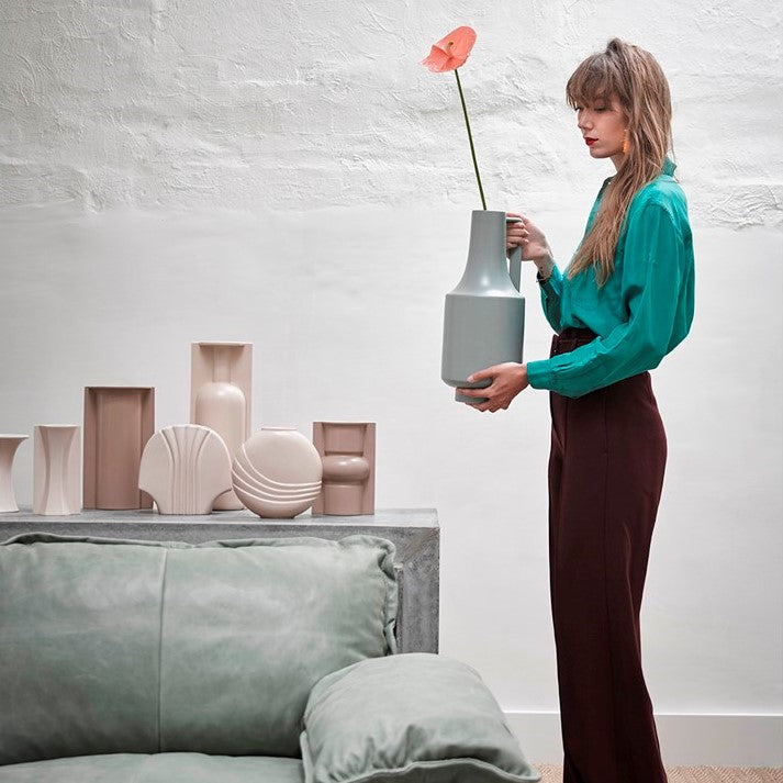 woman with green blouse and brown hair holding a tall green vase with one handle