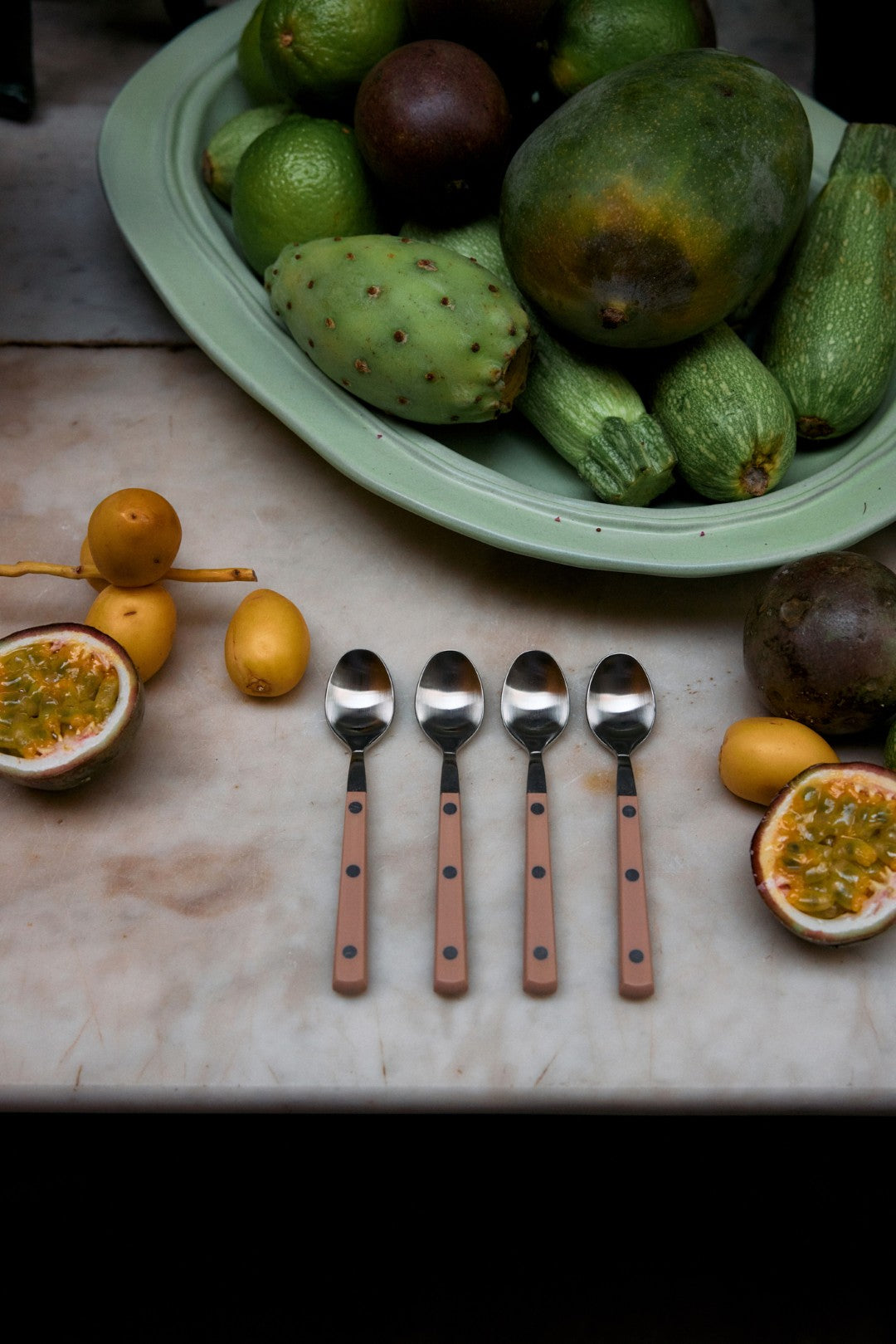 Fruit including avocados and passion fruits on a table with spoons.