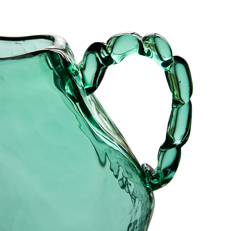 Close-up of a green glass pitcher with a handle on a white background