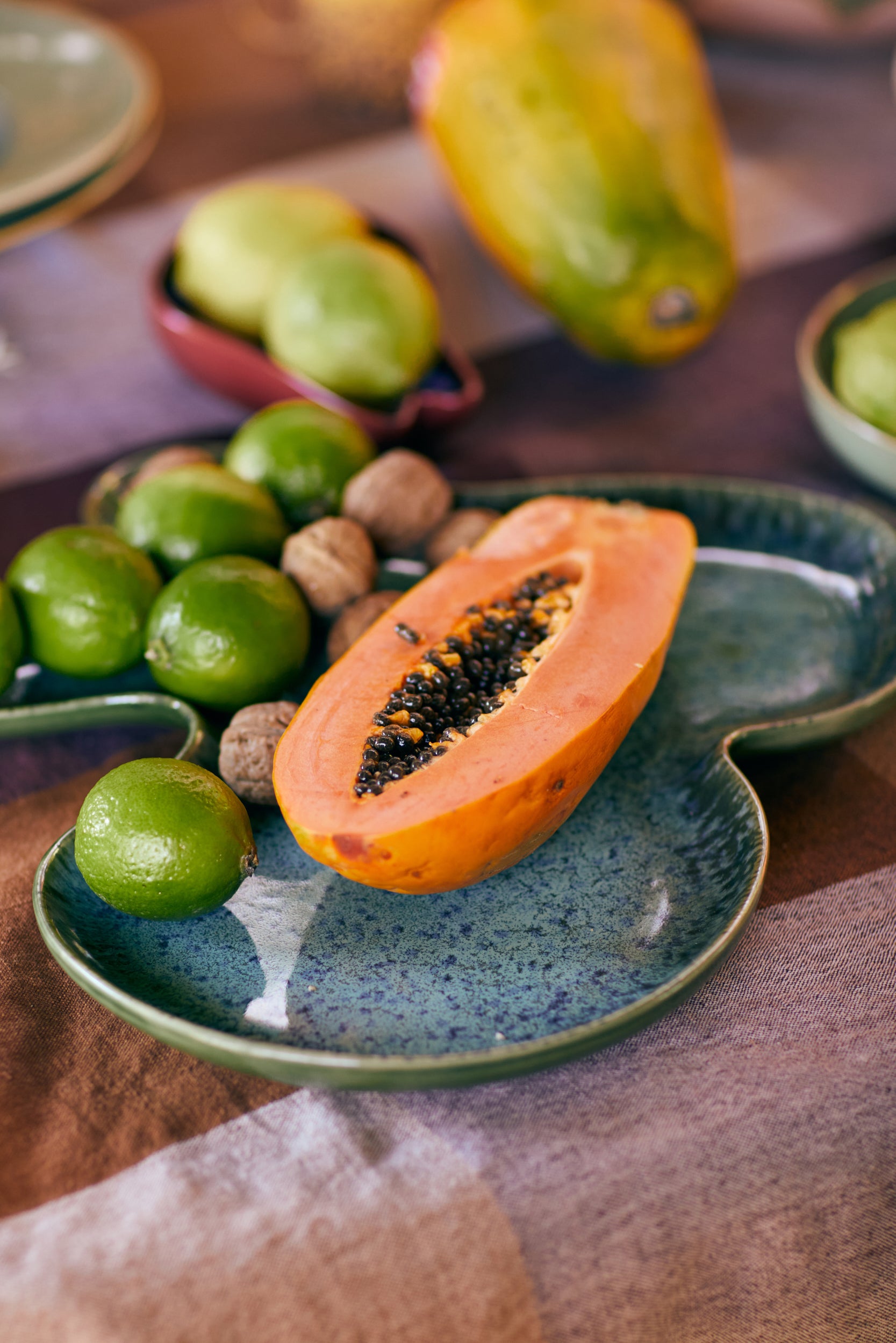 Half-cut papaya on a blue ceramic plate with limes and nuts on a wooden surface.