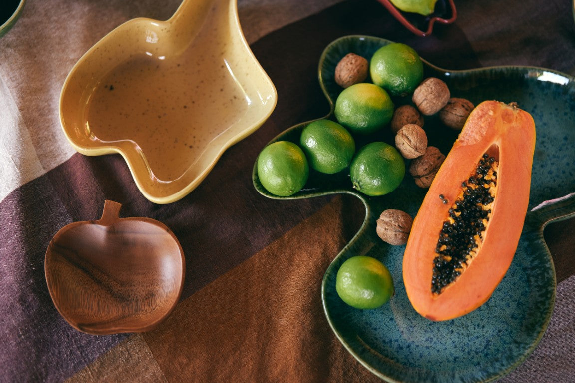 Half-cut papaya on a blue plate with limes and nuts on a brown textured surface