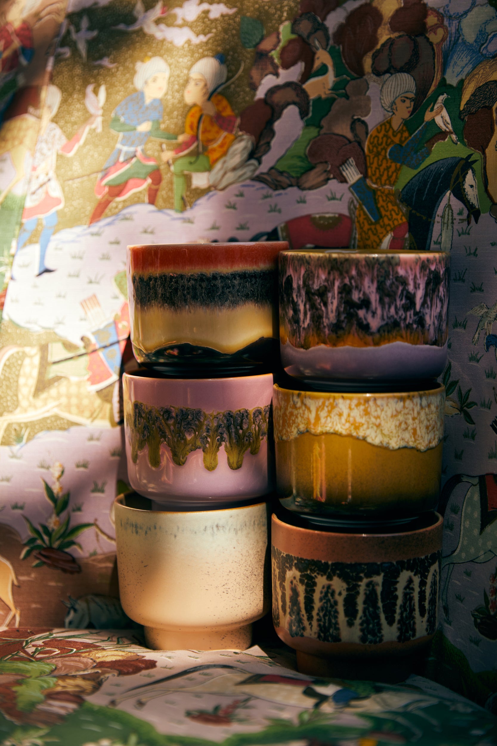 Stack of ceramic pots with textured glazes against a colorful, patterned background