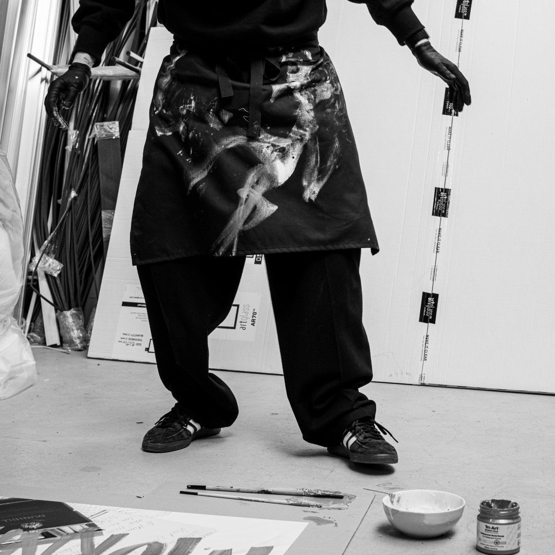 Person wearing a patterned apron in an art studio with paint and canvases.