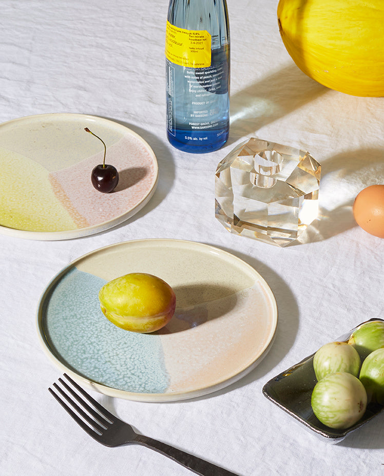 Table setting with ceramic plates, fruit, a bottle, and a crystal on a white surface.