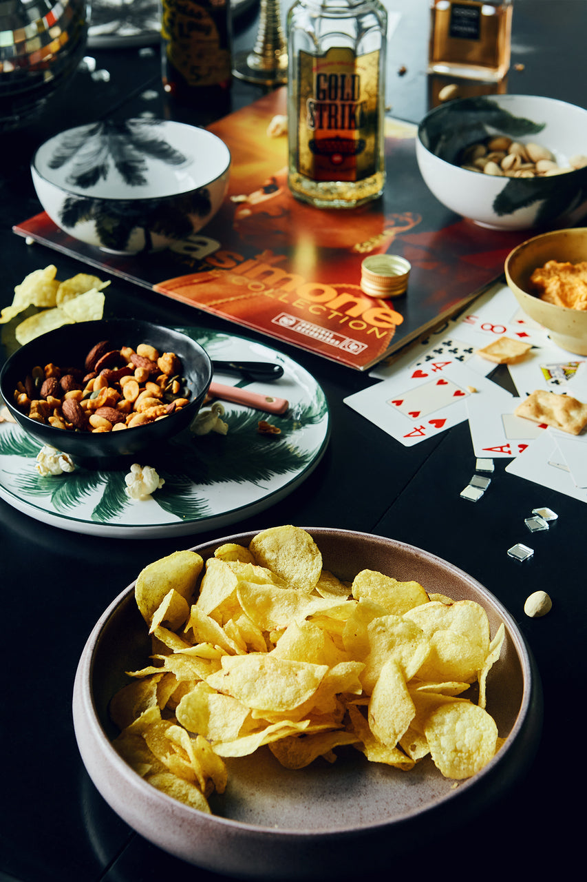 purple plate with potato chips on table with card game and bowl with mixed nuts