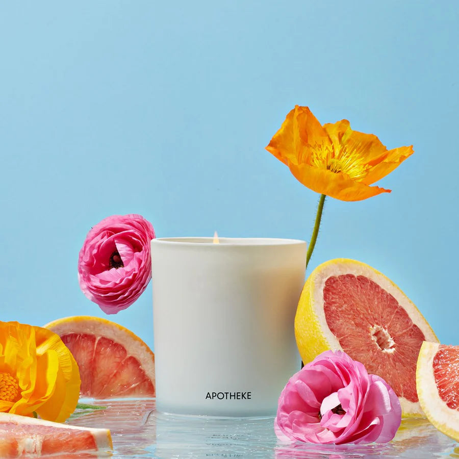 glass vessel with candle and pink flower, grapefruit and blue background