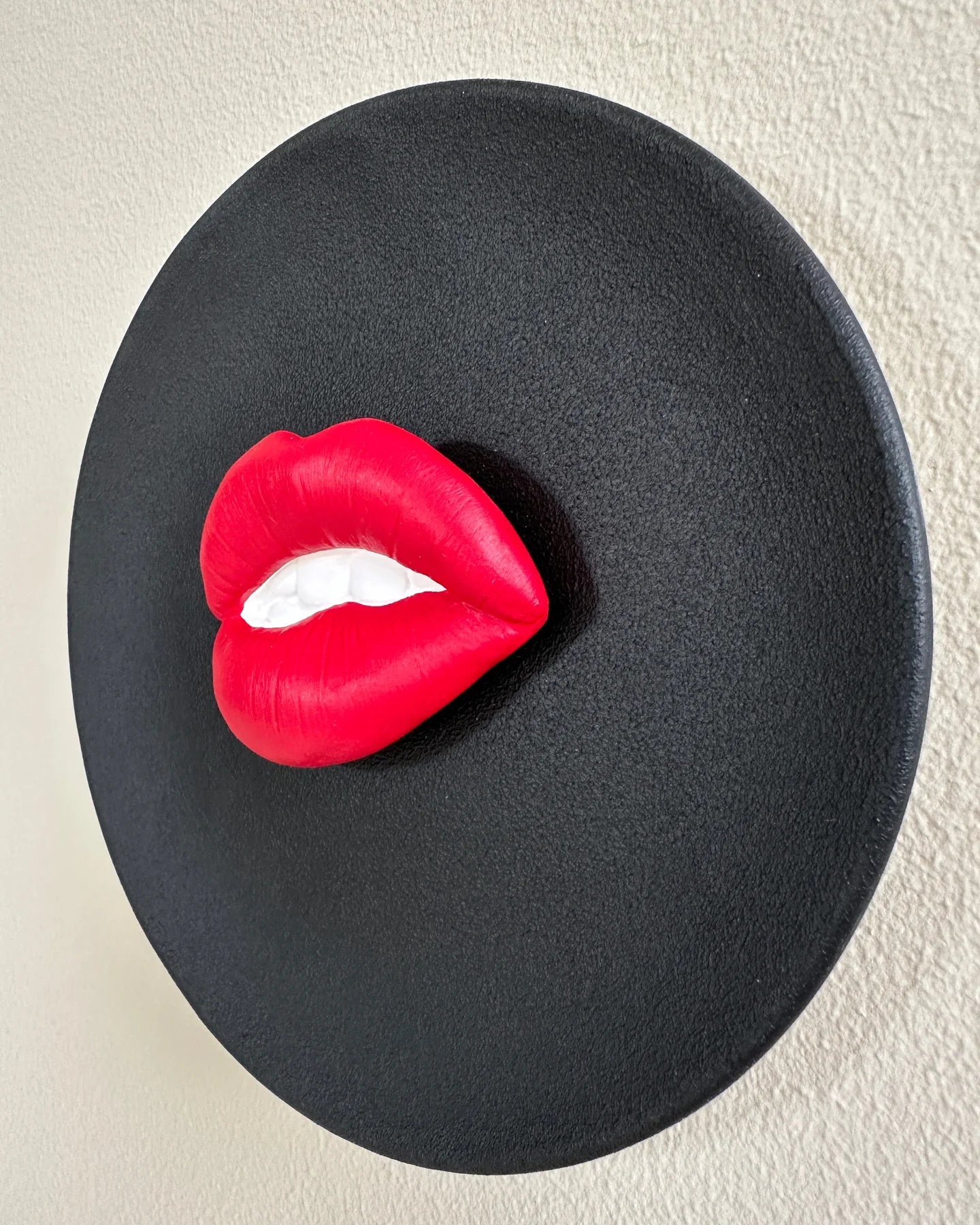 Red lips-shaped object on a black plate against a beige background