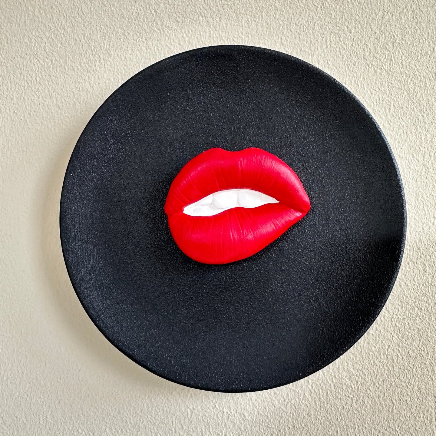 Black plate with red lips on a beige background