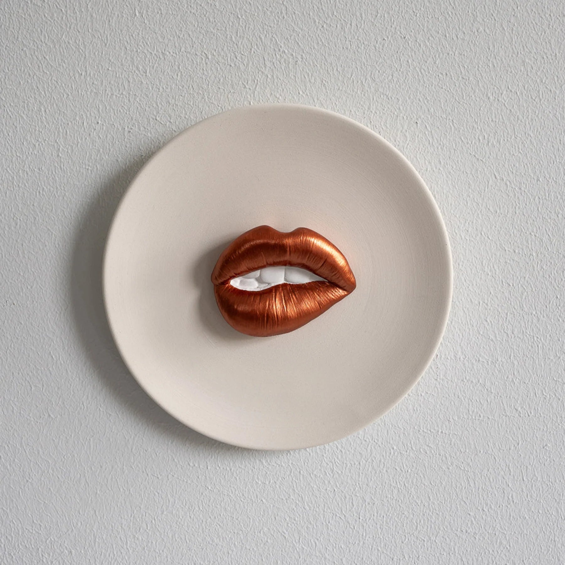 Copper-colored lip-shaped object on a white plate against a light gray background