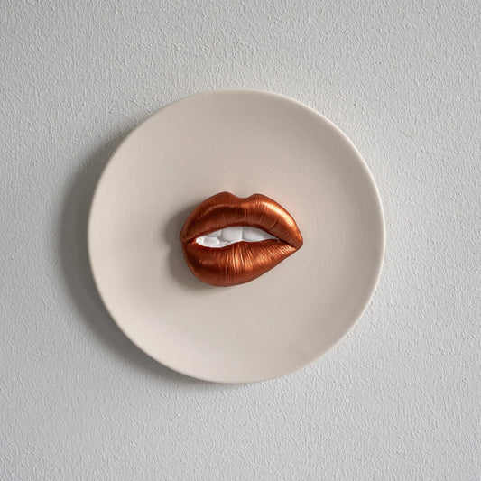 Copper-colored lip-shaped object on a white plate against a light gray background