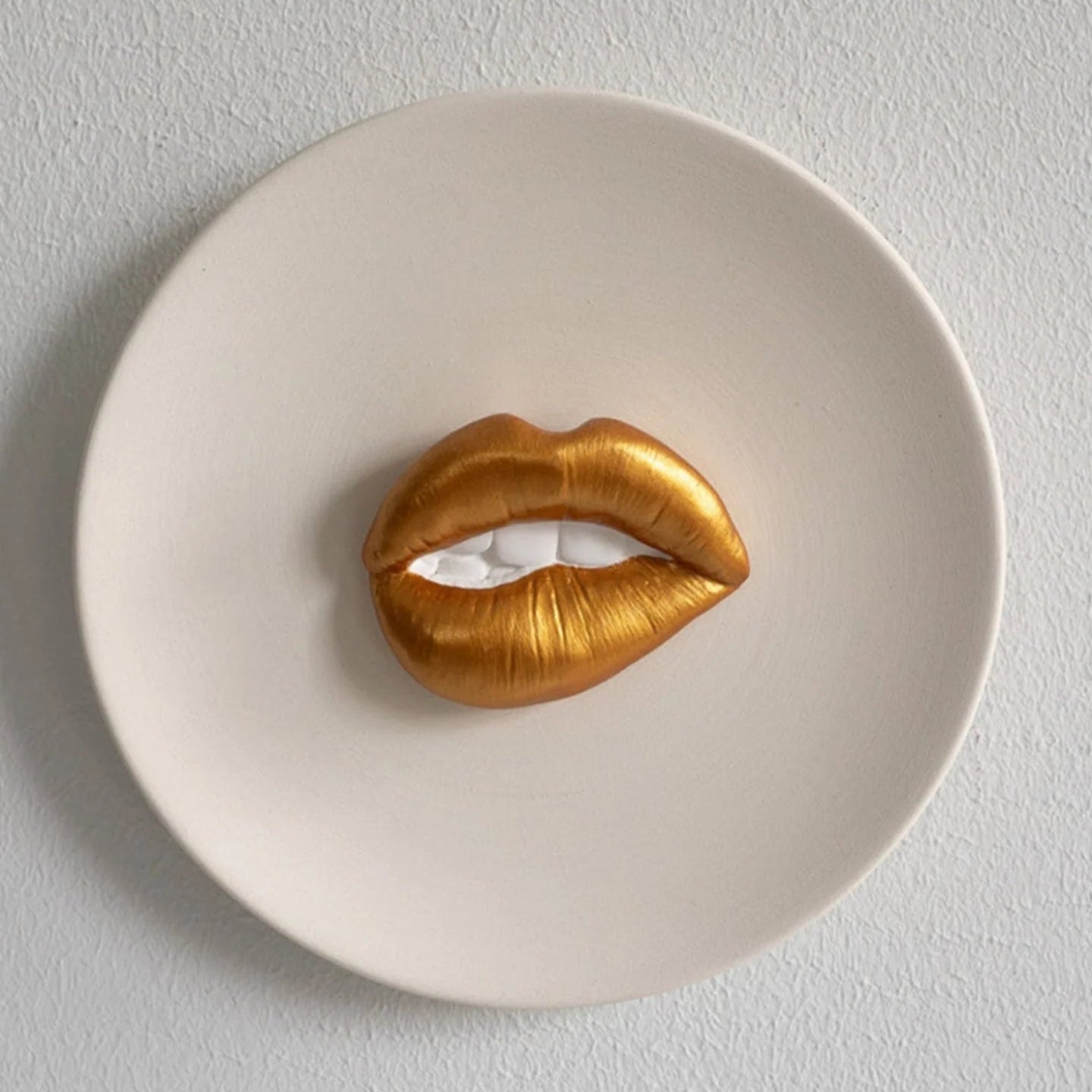 Gold lip-shaped object on a white plate against a light gray background