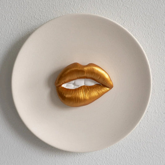 Gold lip-shaped object on a white plate against a light gray background