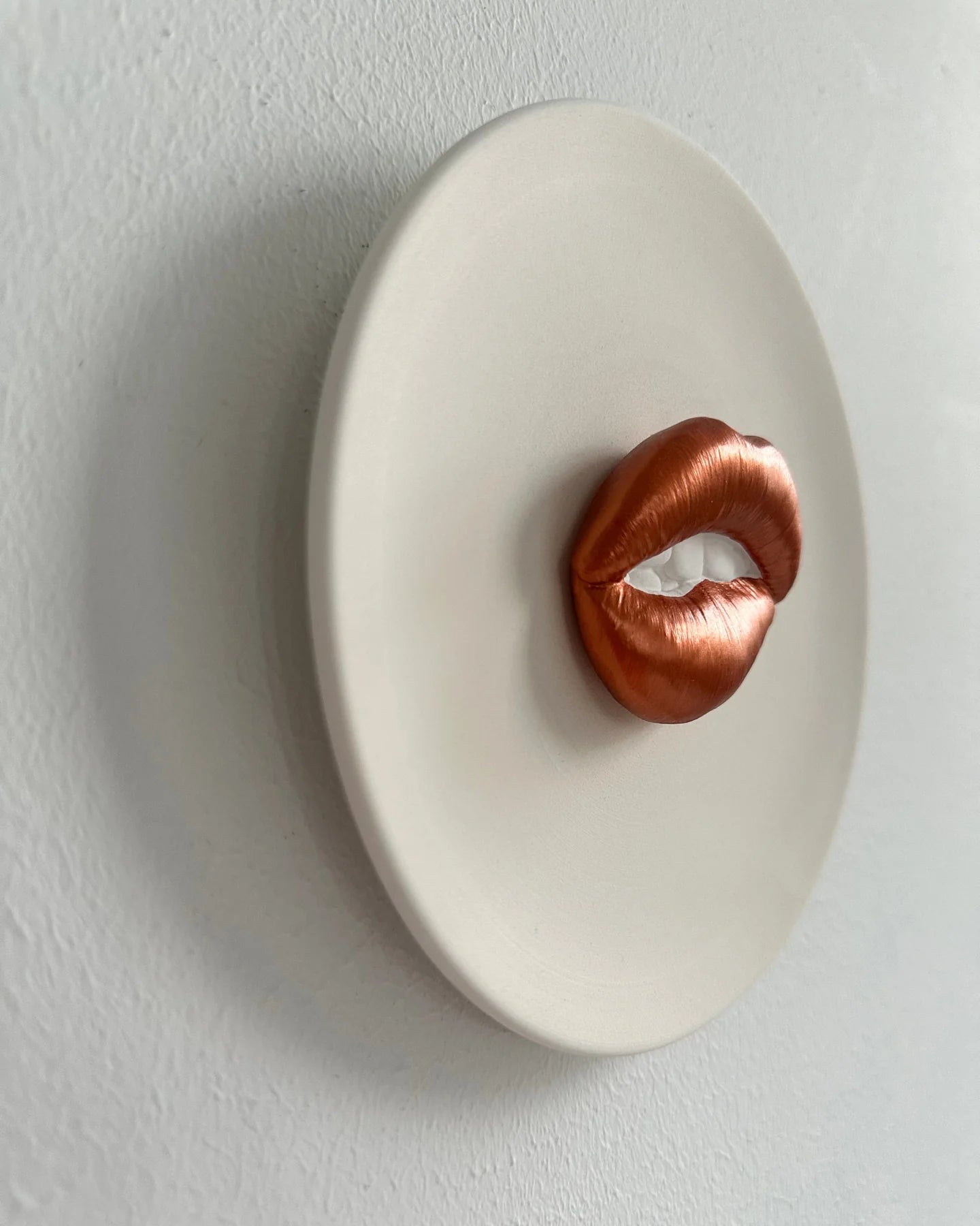 Copper lips sculpture on a white oval plate against a light gray background
