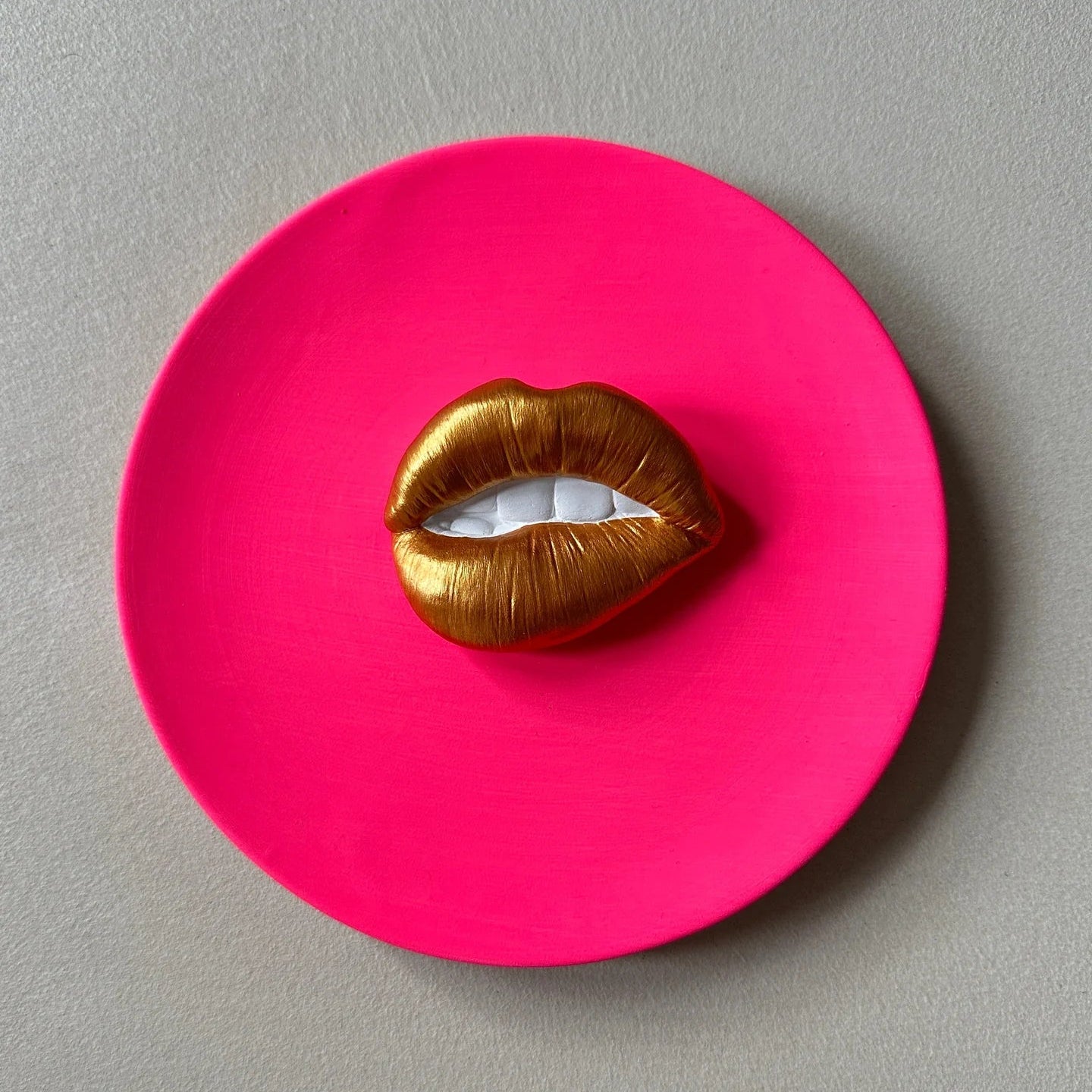 Pink circular object with gold lips on a gray background