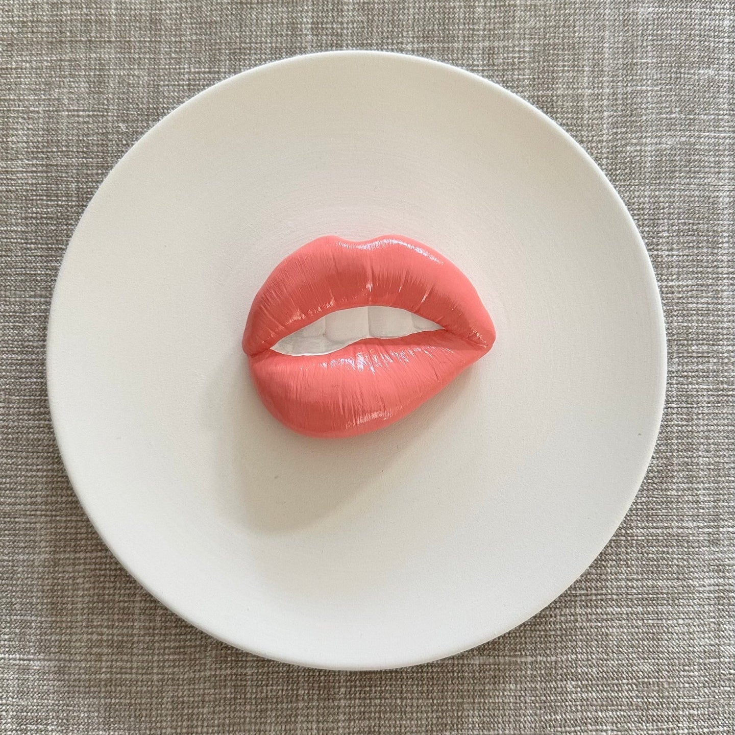 Pink lip-shaped object on a white plate with a textured gray background