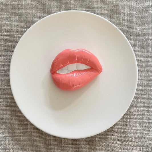 Pink lip-shaped object on a white plate with a textured gray background