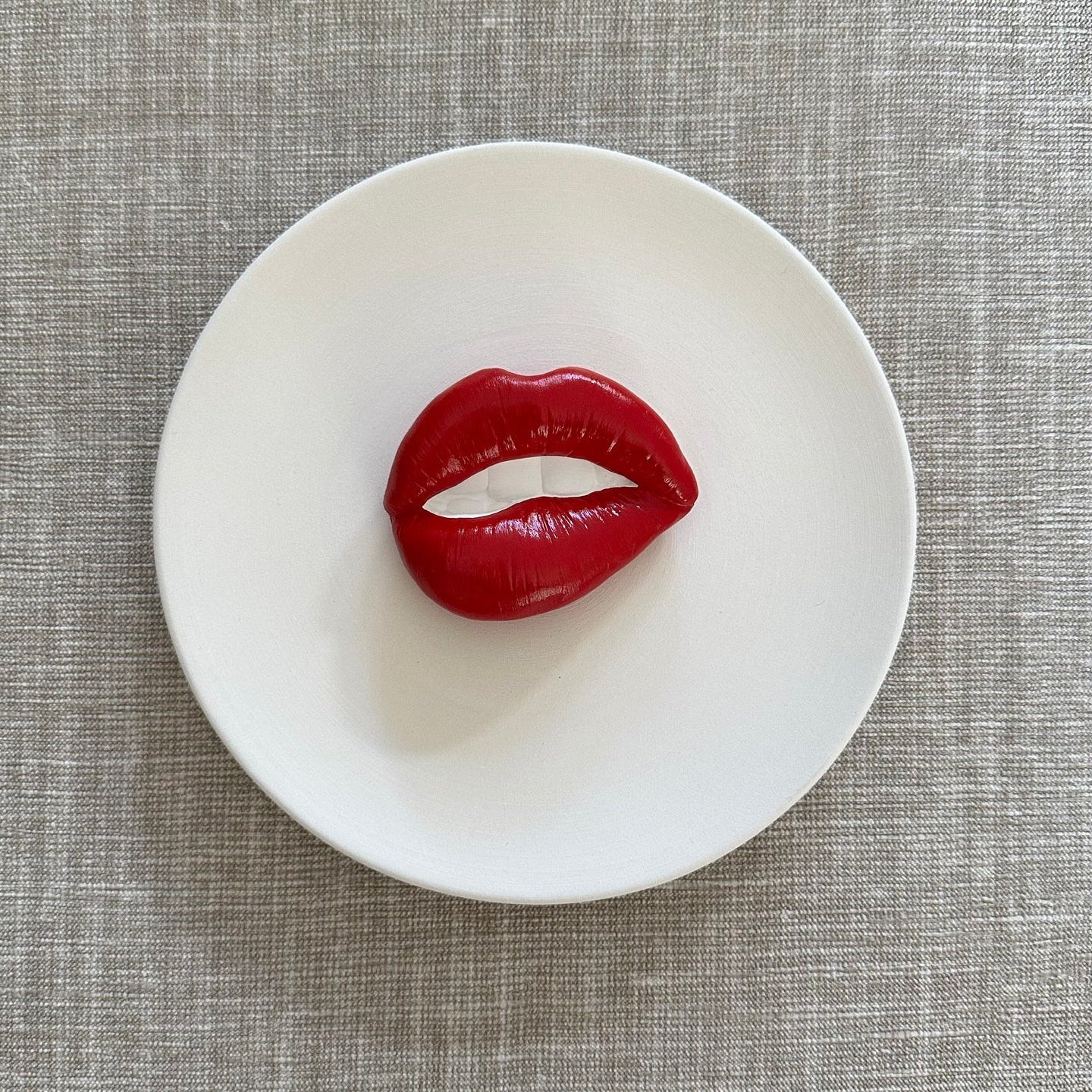 Red lip-shaped object on a white plate with a gray textured background