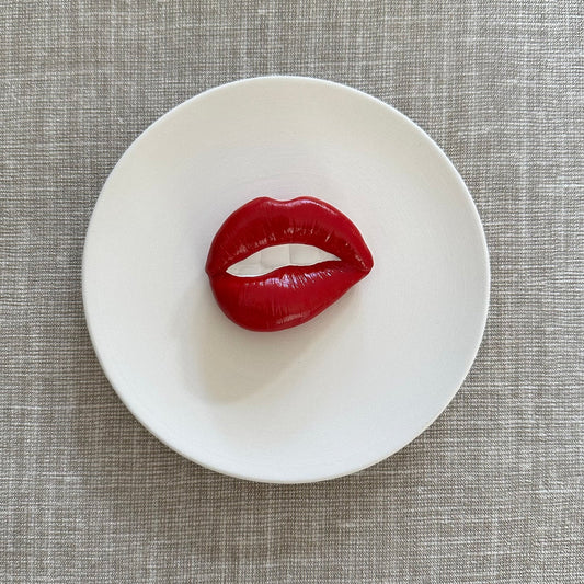 Red lip-shaped object on a white plate with a gray textured background