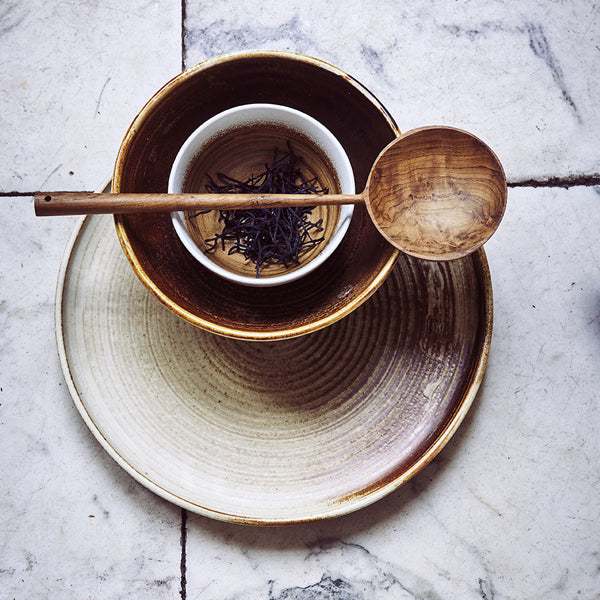 cream and brown color dinner plate, brown dessert plate and cup with tea plus a wooden spoon on top 