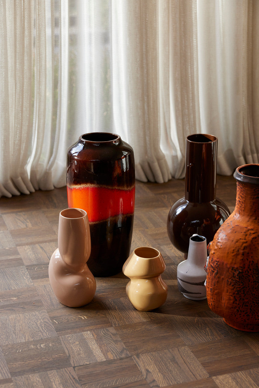 light brown organic shaped vase sculpture among large vases on wooden floor