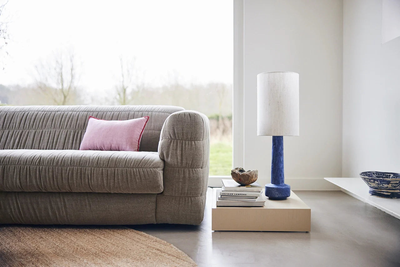 sand colored wooden plateau table with blue table lamp next to a large club sofa