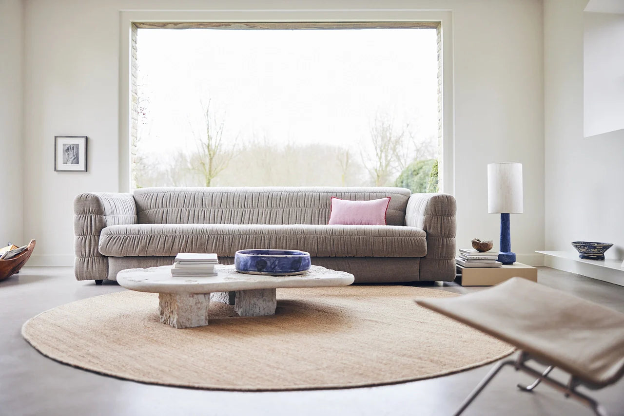 contemporary style club couch in a taupe color fabric that is a mix of linen and cotton in a living room with a blue colored table lamp and a large round hemp area rug