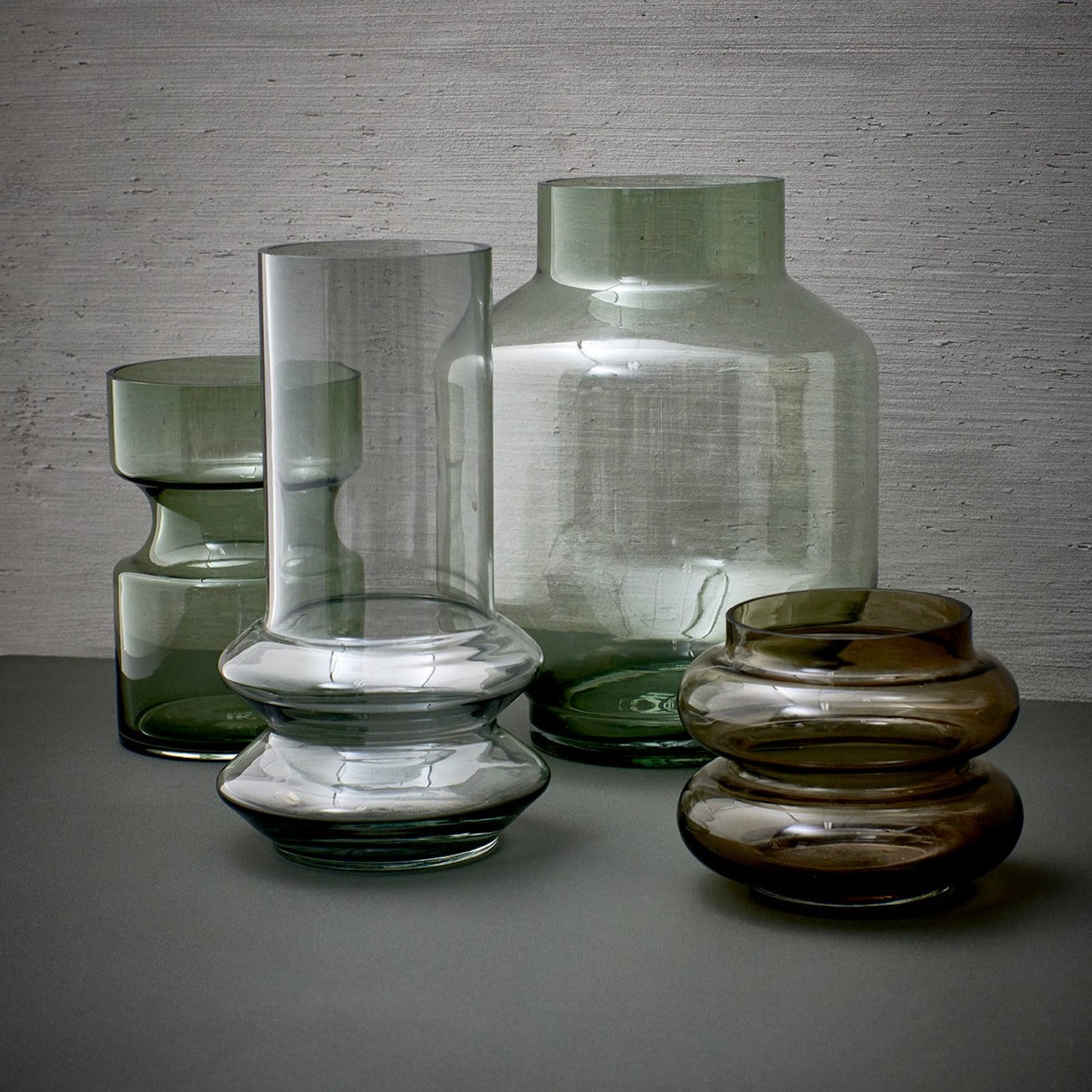 4 glass flower vases iin brown grey and green tones on a charcoal colored table